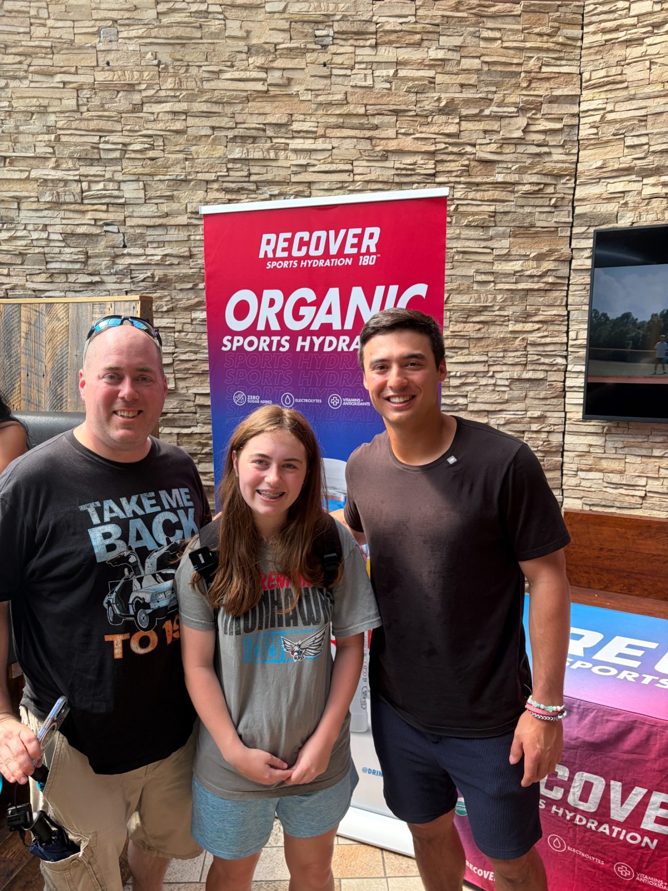 A man and a teenage girl pose for a photo in front of an organic sports apparel banner.
