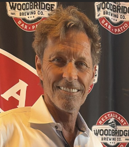 Smiling man with tousled hair against a branded brewery backdrop.