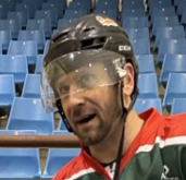 Man in hockey gear wearing a helmet, standing in an empty arena with blue seats.